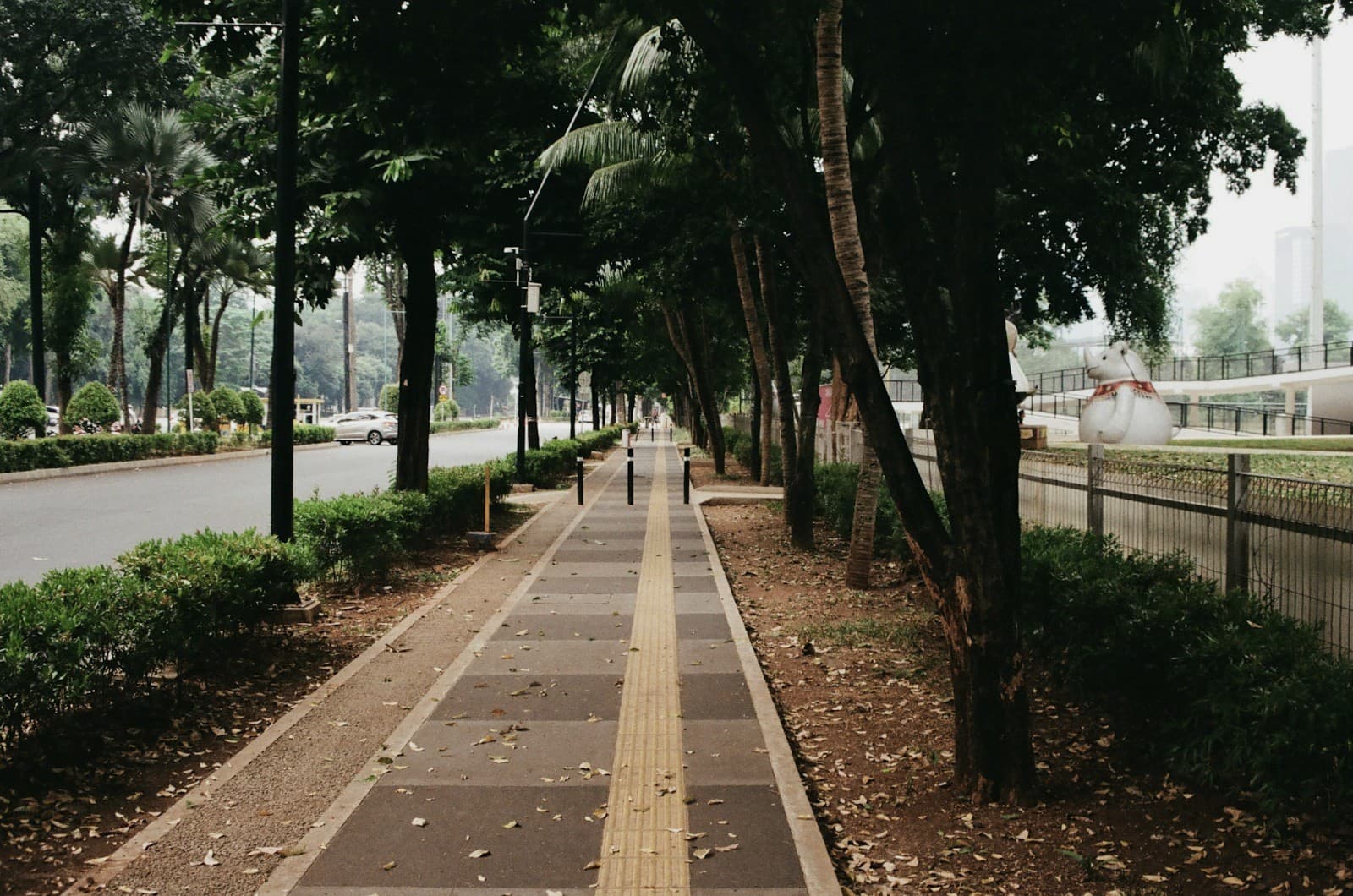 A sidewalk with a yellow tactile guide path and bollards ahead